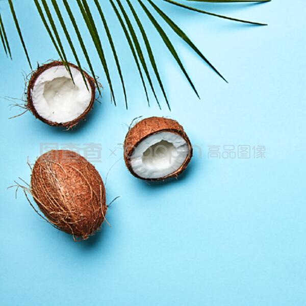 整個和一半的椰子,在藍(lán)色背景上的棕櫚葉和文本空間的副本。一個奇異的水果。扁平放。一個椰子和棕櫚綠葉在藍(lán)色背景上的副本空間。熱帶堅果。扁平放。
